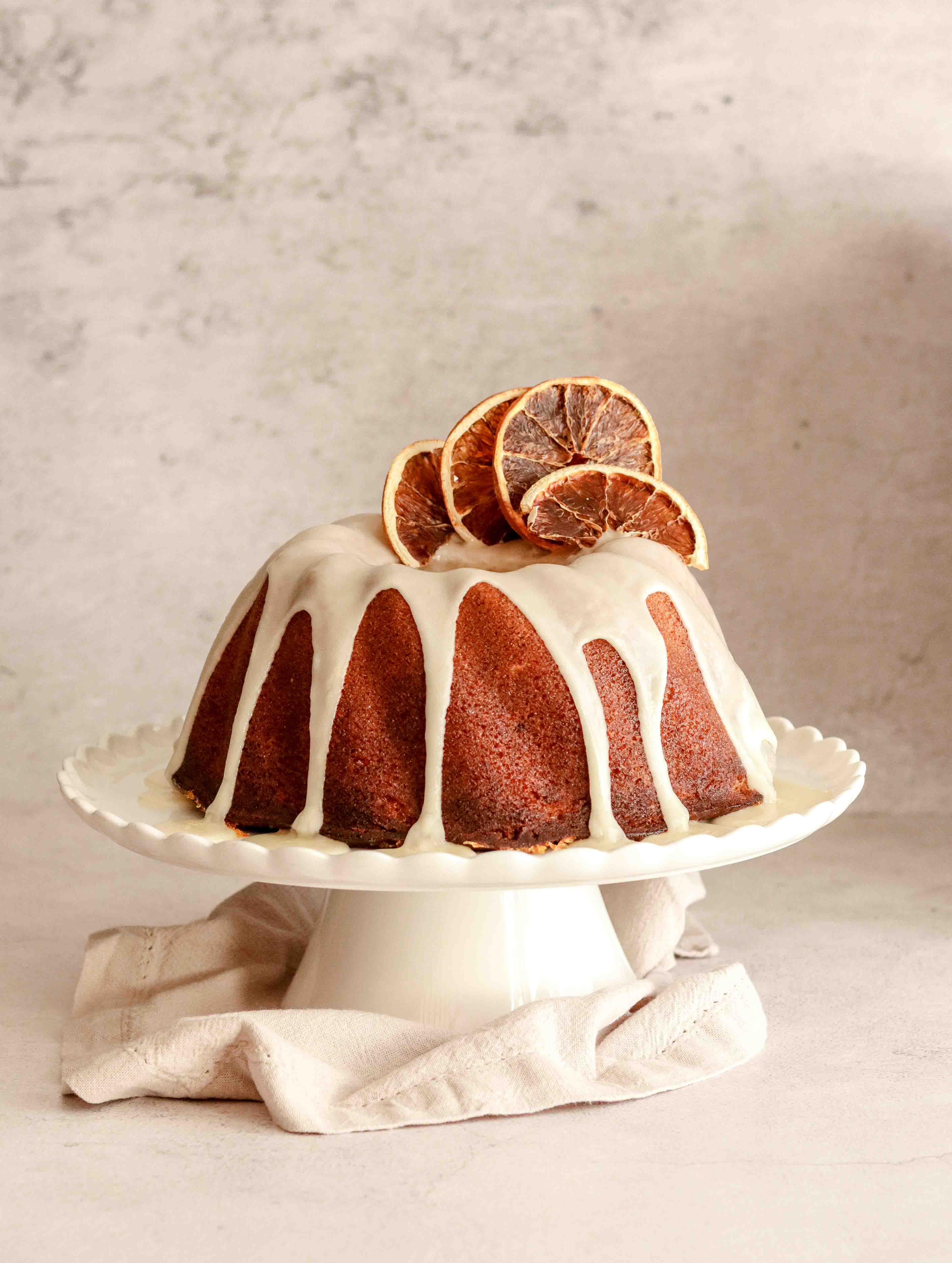 Orange drizzle bundt cake on a white cake stand