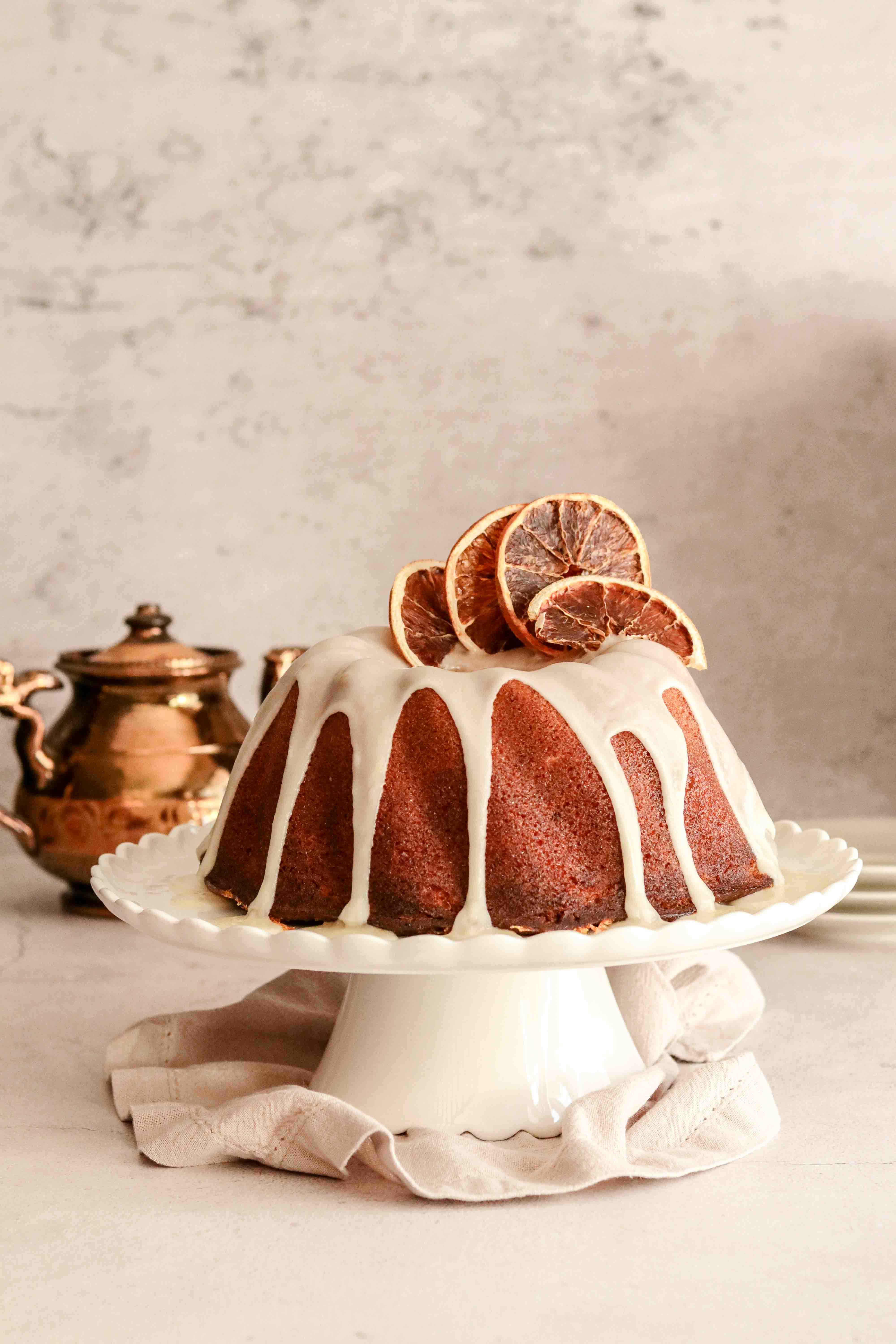 Orange drizzle bundt cake on a white cake stand