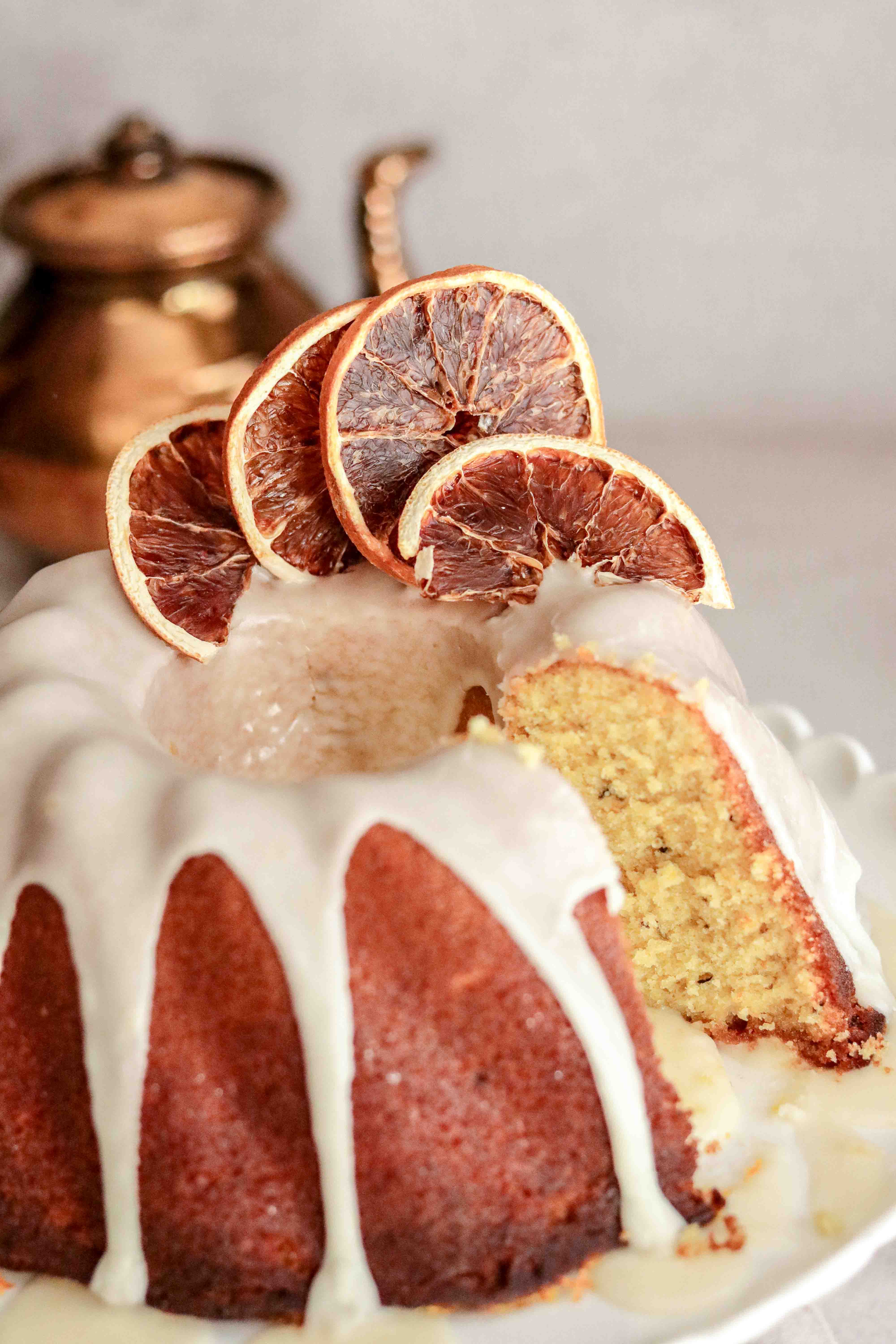 Close up of an orange drizzle bundt cake on a white cake stand